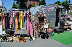 an old trailer with clothes hanging on the rack and other items in front of it