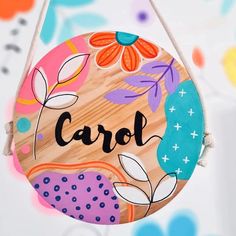 a wooden sign that says carol hanging from a string on a colorful background with flowers and leaves