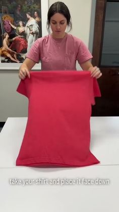 a woman is holding up a piece of pink cloth in front of an art work