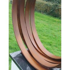 a sculpture in the middle of a grassy area with three curved wooden pieces on top of it