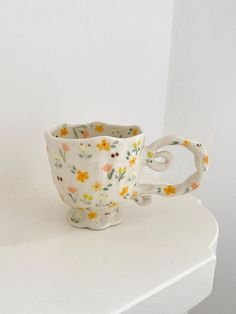 a white cup with yellow and orange flowers on it sitting on a table next to a wall