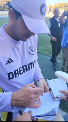 a man signing autographs for fans on the sidelines at a football game with other people in the background