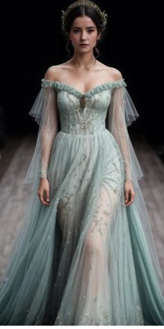 a woman in a blue gown with sheer sleeves and an elaborate headpiece on the runway