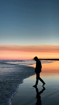 a man walking along the beach at sunset with his reflection in the wet sand as the sun sets