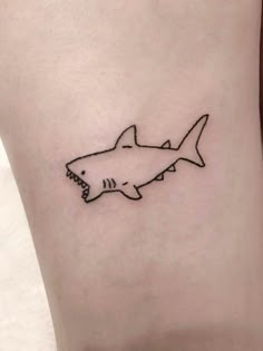 a small shark tattoo on the ankle with black ink and an outline of a shark