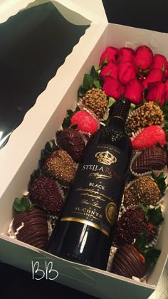 a box filled with chocolate covered strawberries next to a bottle of wine and roses