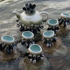 four teapots are sitting on rocks in the water with beads hanging from them