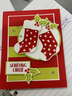 a christmas card with two stockings and holly on the bottom, sitting on top of a pile of papers