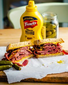 a corned beef sandwich cut in half with pickles and mustard next to it