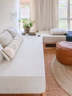 a bed room with a neatly made bed next to a window and a round ottoman