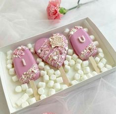 three heart shaped cookies in a box with marshmallows on the table next to flowers