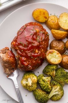 a white plate topped with meat, potatoes and broccoli covered in ketchup