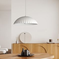 a dining room table and chairs in front of a white wall with an oval light hanging over it