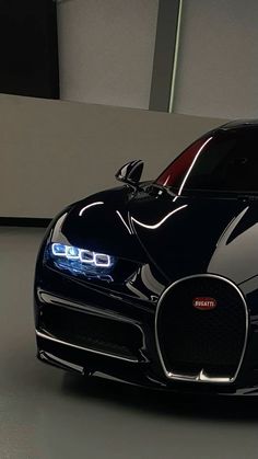 a black bugatti car parked in a garage with its lights on and the hood up