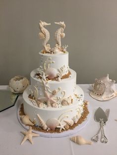 a three tiered wedding cake with seahorses and seashells on top