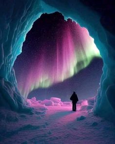 a man standing in front of an ice cave looking at the aurora bore and northern lights