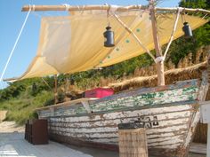 an old boat sitting on top of a sandy beach next to the ocean under a yellow tarp