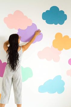 a woman standing in front of a wall with clouds painted on it