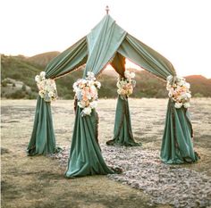 an outdoor wedding setup with green draping and flowers on the side of it