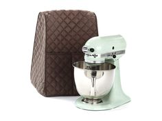 a green mixer sitting next to an oven mitt on a white surface with a brown case behind it