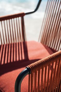 an orange chair sitting on top of a red cushion next to the ocean and water