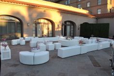 an outdoor seating area with white couches and flower centerpieces in front of a building