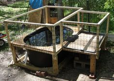 a caged in animal enclosure with a small pond inside it and a wheelbarrow nearby