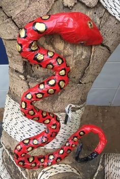 a red snake wrapped in plastic on top of a tree trunk with its mouth open