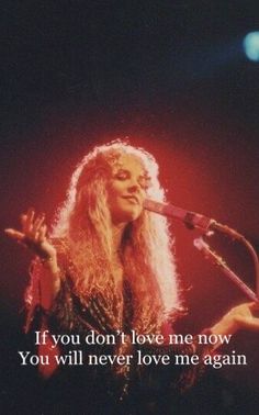 a woman with long hair holding a microphone and singing into a microphone in front of her