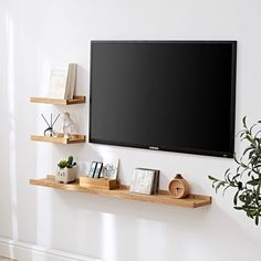 a flat screen tv mounted to the side of a wall next to books and plants