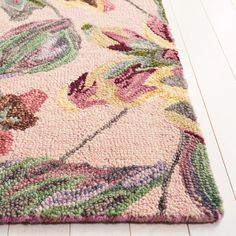 an area rug on the floor with white wood floors and pink flowers in the center