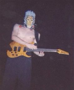 a shirtless man holding an electric guitar in his hand and wearing a costume on