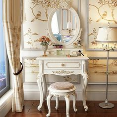 a dressing table with a mirror and stool in front of a wallpapered room