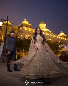 a man and woman posing for a photo in front of a building with lights on it