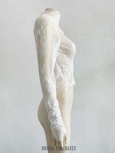 a mannequin wearing a white lace top with long sleeves and openwork on the arms