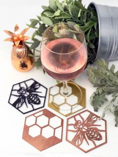 three wine glasses and some metal coasters on a white table with plants in the background