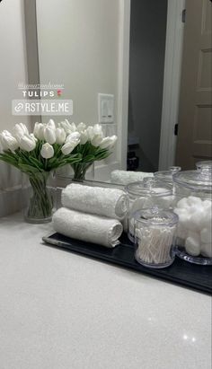 white flowers in a vase on a bathroom counter with towels and candles next to it