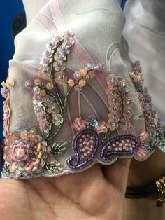 a hand holding a piece of cloth covered in sequins and beads with a flower design on it