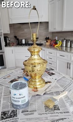 a gold lamp sitting on top of a kitchen counter next to a bucket of paint