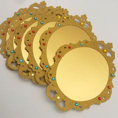 four gold mirrors with colorful beads on them sitting next to each other in front of a white background