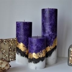 three purple and gold pillar candles sitting next to each other on a white table with beads