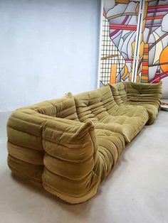 a very long couch sitting in front of a colorful painting on the side of a wall