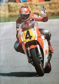 a man riding on the back of a motorcycle down a race track with his hand in the air