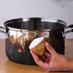 a person is holding a piece of food in front of a pot on a table