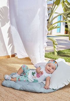 a baby laying on top of a blue blanket next to a white curtain and potted plant