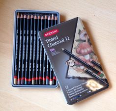 two tins of colored pencils sitting next to each other on top of a wooden table