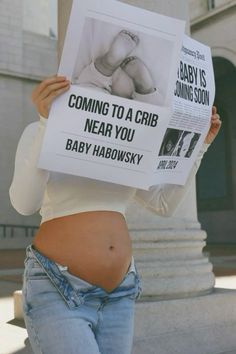 a pregnant woman holding up a newspaper with the caption baby is coming to a crib near you