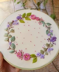 a hand holding a white plate with pink and purple flowers painted on the side, in front of a brick wall