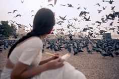 a woman sitting in front of a flock of birds