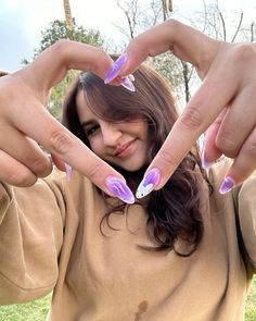 a woman with purple and white nail polish holding her hands in the shape of a heart